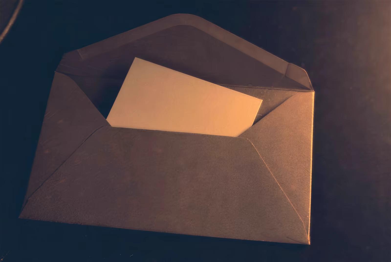 A blank card halfway out of a kraft envelope under warm lamp light
